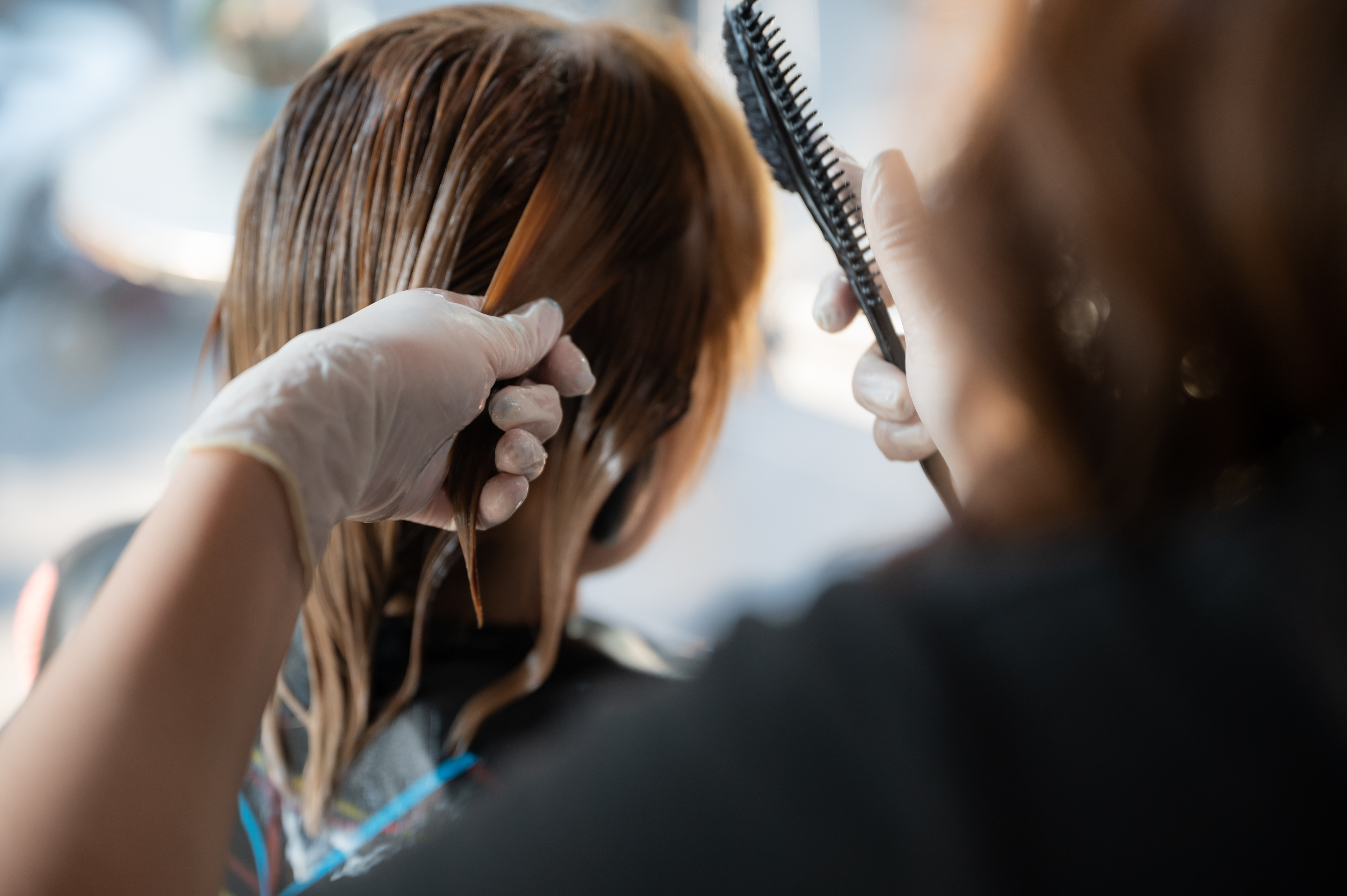 hairstylist wearing gloves applying product to wet hair using a comb and hands in a salon
